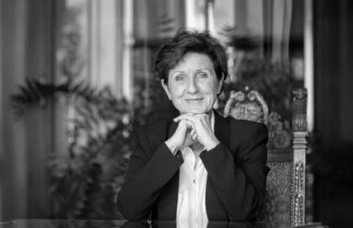 czarnobiały portret kobiety w dojrzałym wieku, uśmiechnięta, podbierająca splecionymi dłońmi brodę